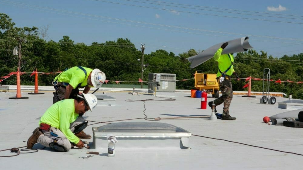 Crew rolling out and detailing white membrane on a low-slope commercial roof